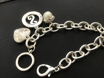 Sale Photo Thumbnail #102: Silver-tone chain charm bracelet featuring three charms: an embossed heart, a rhinestone-accented initial 'S' medallion, and a faux pearl drop. Features both a lobster claw clasp and a decorative ring clasp section. In good pre-owned condition with light 