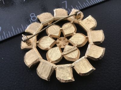 Sale Photo Thumbnail #67: A vintage gold-tone floral brooch featuring vibrant blue and green enamel accents. Marked 'FLORENZA ©' on the back with a secure roll-over safety clasp. Measures approximately 1.75 inches in diameter. In good vintage condition with minor surface wear con