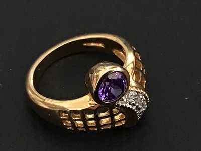 Sale Photo Thumbnail #246: A distinctive gold-tone statement ring featuring a bypass-style lattice/grid design, accent stones along the band, and a bezel-set purple round stone. Shown on a ring mandrel measuring approximately size 6 to 6.5. Good condition with light surface wear.