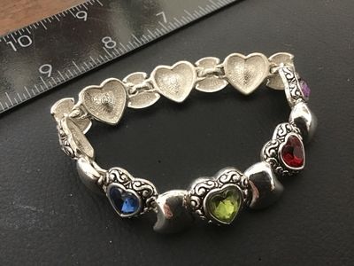Sale Photo Thumbnail #66: Silver-tone costume jewelry link bracelet featuring heart-shaped scrollwork links set with vibrant multi-colored heart crystals (red, purple, blue, green). Measures approximately 7.5 to 8 inches in length. In good condition with light surface wear.
