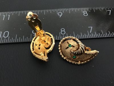 Sale Photo Thumbnail #145: Pair of vintage gold-tone textured paisley swirl clip-on earrings featuring small green rhinestone accents. Each earring measures approximately 1 inch long. In good vintage condition with minor surface wear consistent with age.