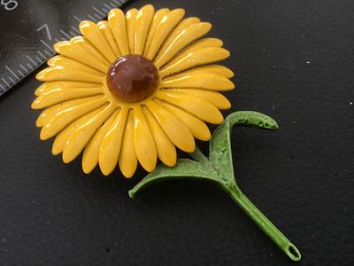 Sale Photo Thumbnail #90: A mid-century style vintage enamel brooch in the shape of a yellow flower with a brown center dome and green stem/leaves. Made of painted/enameled metal. Pin back attachment is intact. Measures approximately 3 inches across. Shows minor finish wear and li