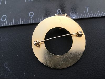 Sale Photo Thumbnail #59: Vintage circular gold-tone brooch featuring textured, engine-turned design details, accented with a single faux pearl and a prong-set faceted deep purple stone/glass element. Includes a standard pin mechanism on the reverse. Shows minor surface wear consi