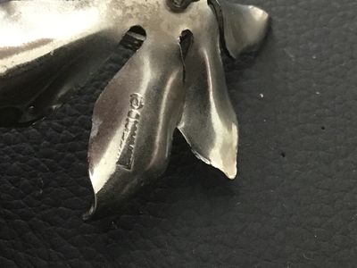 Sale Photo Thumbnail #124: A vintage silver-tone floral brooch Signed  featuring textured, vein-detailed leaves surrounding a domed, textured center. Marked on the back with the copyright Sarah Cov signature. Measures approximately 2 inches wide. Shows minor vintage surface wear co