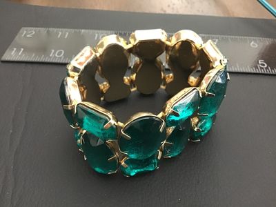 Sale Photo Thumbnail #159: A striking wide stretch cuff bracelet featuring large, prong-set emerald-green faceted glass or acrylic stones set in gold-tone metal. The bracelet design stretches for adjustable sizing and measures approximately 2 inches in width. Shows light wear consi