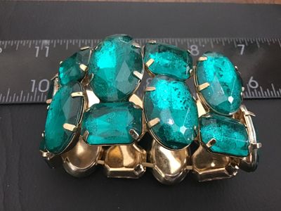 Sale Photo Thumbnail #156: A striking wide stretch cuff bracelet featuring large, prong-set emerald-green faceted glass or acrylic stones set in gold-tone metal. The bracelet design stretches for adjustable sizing and measures approximately 2 inches in width. Shows light wear consi