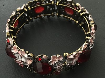 Sale Photo Thumbnail #89: A ornate stretch cuff bracelet featuring antiqued brass-tone metal set with large faceted red glass or acrylic stones, accent rhinestones, and delicate enameling on floral motifs in shades of pink, white, and grey. The bracelet features an elastic stretch
