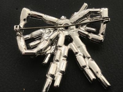 Sale Photo Thumbnail #55: A vintage silver-tone costume jewelry brooch in a dimensional bow design, set with baguette and round cut clear rhinestones. Features a pin stem and roll-over safety clasp on the reverse. Measures approximately 2 inches wide by 2 inches long. Good vintage