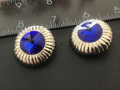 Sale Photo Thumbnail #121: Pair of vintage round silver-tone clip-on earrings featuring prominent faceted cobalt blue  center  set in a ribbed dome border. Textured textured backs with clip fastenings. Each earring measures approximately 1 inch in diameter. Show light age-appropria