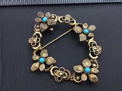 Sale Photo Thumbnail #160: Vintage gold-tone openwork wreath brooch featuring embossed flowers accented with round turquoise-colored cabochons. Includes a rollover C-clasp pin back and an integrated pendant bail on the reverse for dual wear as a brooch or pendant. Measures approxim