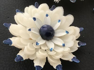 Sale Photo Thumbnail #138: Matching 3-piece vintage jewelry set featuring a large floral brooch pin and two clip-on earrings. Crafted from layered white celluloid petals with painted blue tips and a dark blue center cabochon accent. Brooch measures approximately 3.5 inches across. 