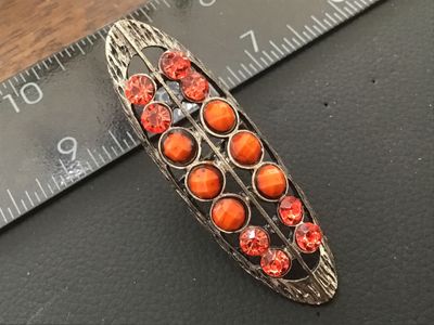 Sale Photo Thumbnail #81: Elongated statement ring featuring a textured silvertone openwork setting encrusted with faceted orange rhinestones and opaque orange cabochon/bead accents. Features an adjustable band on the back. The top measures approximately 2.5 inches in length. In g
