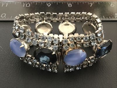 Sale Photo Thumbnail #42: Vintage wide costume jewelry bracelet featuring alternating faceted dark blue rhinestones and light blue opaque oval cabochons set between double rows of clear rhinestones. Silver-tone metal setting with a fold-over clasp. Measures approximately 7 inches 