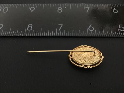 Sale Photo Thumbnail #171: A vintage gold-tone stickpin featuring an oval carved shell cameo depicting a woman in profile. The cameo is set in a decorative ornate filigree and rope-edge frame. The back of the setting features detailed scrollwork and filigree design. Total length me