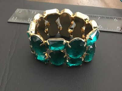 Sale Photo Thumbnail #157: A striking wide stretch cuff bracelet featuring large, prong-set emerald-green faceted glass or acrylic stones set in gold-tone metal. The bracelet design stretches for adjustable sizing and measures approximately 2 inches in width. Shows light wear consi