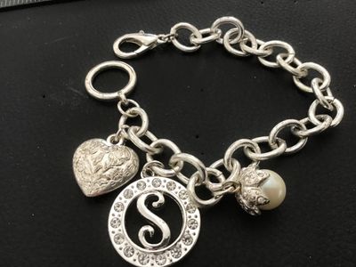 Sale Photo Thumbnail #101: Silver-tone chain charm bracelet featuring three charms: an embossed heart, a rhinestone-accented initial 'S' medallion, and a faux pearl drop. Features both a lobster claw clasp and a decorative ring clasp section. In good pre-owned condition with light 