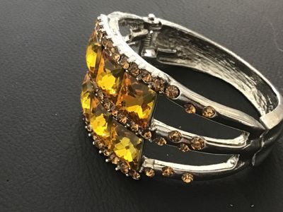 Sale Photo Thumbnail #116: Silver-tone metal hinged cuff bracelet featuring six large square-cut yellow/amber faux crystal central stones bordered by smaller amber-colored rhinestones. Features a spring-hinged closure. Good pre-owned condition with minor finish wear to the reverse.