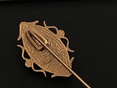 Sale Photo Thumbnail #175: Vintage gold-tone stick pin featuring an oval faux-cameo with a white profile against a terracotta-red background, surrounded by a scrolled frame accent with four small faux pearls. Signed "© SARAH COV" on the back. Measures approximately 3 inches in tot