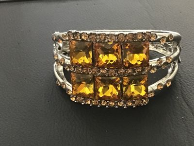 Sale Photo Thumbnail #115: Silver-tone metal hinged cuff bracelet featuring six large square-cut yellow/amber faux crystal central stones bordered by smaller amber-colored rhinestones. Features a spring-hinged closure. Good pre-owned condition with minor finish wear to the reverse.