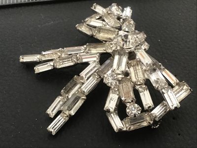 Sale Photo Thumbnail #54: A vintage silver-tone costume jewelry brooch in a dimensional bow design, set with baguette and round cut clear rhinestones. Features a pin stem and roll-over safety clasp on the reverse. Measures approximately 2 inches wide by 2 inches long. Good vintage