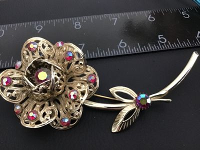 Sale Photo Thumbnail #153: Vintage gold-tone flower brooch by Sarah Coventry featuring ornate filigree work accenting pink/fuchsia aurora borealis rhinestones. Signed "© SARAH COV" on the back stem. Features a secure pin back clasp. Measures approximately 3 inches long. In good vi