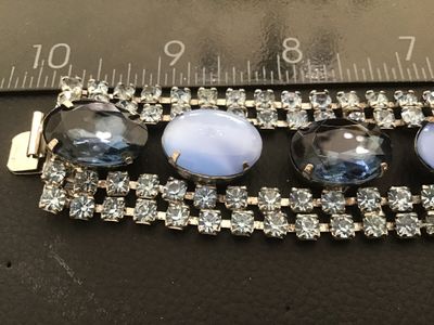 Sale Photo Thumbnail #40: Vintage wide costume jewelry bracelet featuring alternating faceted dark blue rhinestones and light blue opaque oval cabochons set between double rows of clear rhinestones. Silver-tone metal setting with a fold-over clasp. Measures approximately 7 inches 