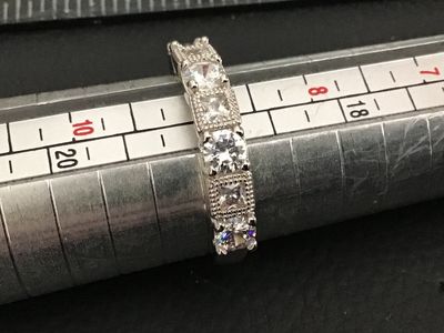 Sale Photo Thumbnail #231: Silver-tone band ring set with five clear cubic zirconia or crystal stones featuring alternating round and square shapes with milgrain border details. Measures approximately size 8 on a ring mandrel. Good condition with minimal wear.