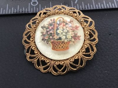 Sale Photo Thumbnail #93: Vintage round filigree brooch pin featuring a central cabochon decorated with a printed floral flower basket design. The gold-tone brass or alloy frame features ornate openwork filigree hearts and dots. Marked 'WESTERN GERMANY' on the back bar mechanism. 