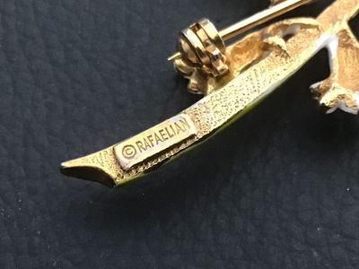 Sale Photo Thumbnail #20: Vintage Rafaelian floral pin featuring white enamel bell-shaped flowers on a green enamel stem with gold-tone backing and detail. Stamped '© RAFAELIAN' on the reverse. Features a standard pin back with a rotating clasp mechanism. Shows minor signs of vin