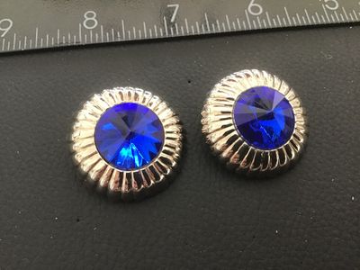 Sale Photo Thumbnail #120: Pair of vintage round silver-tone clip-on earrings featuring prominent faceted cobalt blue  center  set in a ribbed dome border. Textured textured backs with clip fastenings. Each earring measures approximately 1 inch in diameter. Show light age-appropria