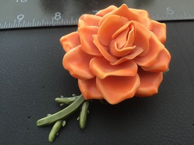 Sale Photo Thumbnail #29: Vintage dimensional orange rose brooch crafted from molded celluloid/plastic material with green stem and leaves on the back. Features a safety pin style clasp mechanism attached to the back. Measures approximately 2.5 inches across. Good pre-owned vintag