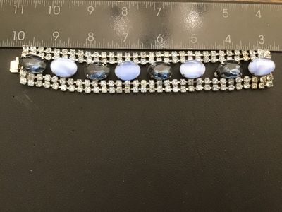 Sale Photo Thumbnail #37: Vintage wide costume jewelry bracelet featuring alternating faceted dark blue rhinestones and light blue opaque oval cabochons set between double rows of clear rhinestones. Silver-tone metal setting with a fold-over clasp. Measures approximately 7 inches 