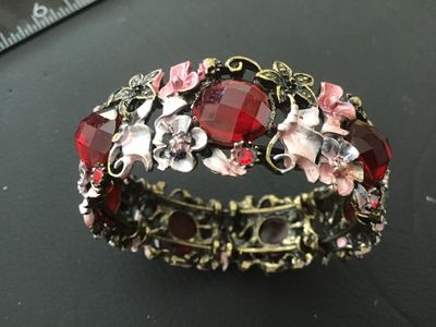 Sale Photo Thumbnail #88: A ornate stretch cuff bracelet featuring antiqued brass-tone metal set with large faceted red glass or acrylic stones, accent rhinestones, and delicate enameling on floral motifs in shades of pink, white, and grey. The bracelet features an elastic stretch