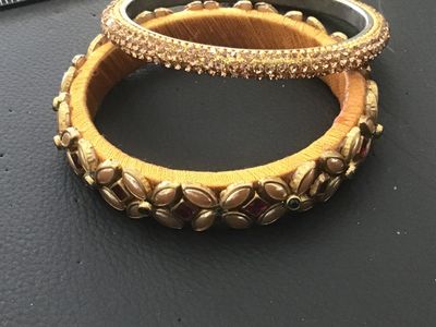 Sale Photo Thumbnail #132: Set of two statement bangle bracelets featuring yellow thread wrapping. One wider bangle is adorned with gold-tone leaf accents, pink/red and green rhinestones, and faux pearl details. The second thinner bangle features full rows of shimmering champagne/g