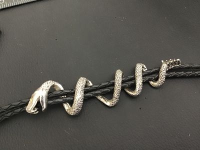 Sale Photo Thumbnail #251: Unique western bolo tie featuring a silver-tone coiling snake slide piece wrapped around a braided black leather/synthetic cord with silver-tone tips. Shows detailed scale texturing and open mouth snake design. Good condition with light wear.