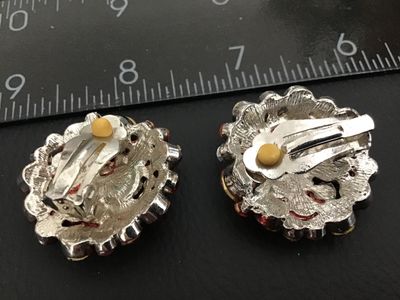 Sale Photo Thumbnail #150: Pair of vintage round clip-on earrings featuring silver-tone metal backing with comfort pads. Decorative floral/sunburst setting set with colorful rhinestones. Each measures approximately 1 inch in diameter based on ruler shown. Good vintage condition wit