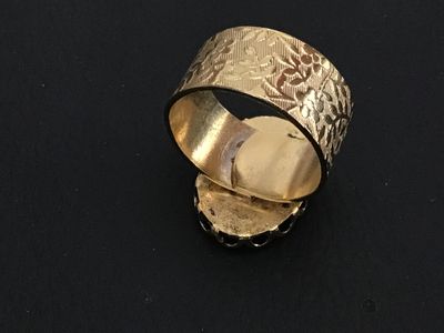 Sale Photo Thumbnail #199: A vintage costume jewelry ring featuring a blue glass molded cameo depicting a classic portrait profile. Set in a scalloped bezel with a wide gold-tone band decorated with an etched floral leaf pattern. Ring measures approximately size 8.5 to 8.75 on a ri