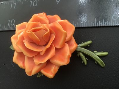 Sale Photo Thumbnail #32: Vintage dimensional orange rose brooch crafted from molded celluloid/plastic material with green stem and leaves on the back. Features a safety pin style clasp mechanism attached to the back. Measures approximately 2.5 inches across. Good pre-owned vintag