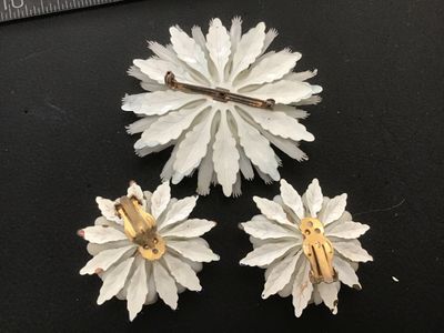 Sale Photo Thumbnail #137: Matching 3-piece vintage jewelry set featuring a large floral brooch pin and two clip-on earrings. Crafted from layered white celluloid petals with painted blue tips and a dark blue center cabochon accent. Brooch measures approximately 3.5 inches across. 