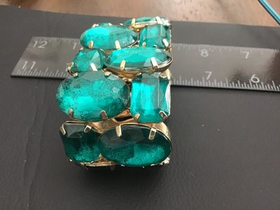 Sale Photo Thumbnail #158: A striking wide stretch cuff bracelet featuring large, prong-set emerald-green faceted glass or acrylic stones set in gold-tone metal. The bracelet design stretches for adjustable sizing and measures approximately 2 inches in width. Shows light wear consi