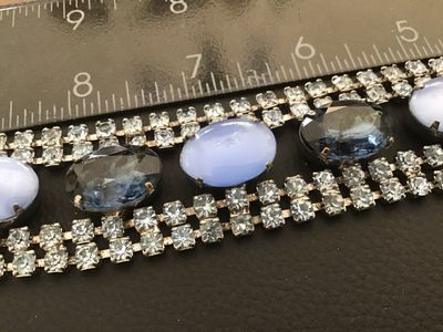 Sale Photo Thumbnail #38: Vintage wide costume jewelry bracelet featuring alternating faceted dark blue rhinestones and light blue opaque oval cabochons set between double rows of clear rhinestones. Silver-tone metal setting with a fold-over clasp. Measures approximately 7 inches 