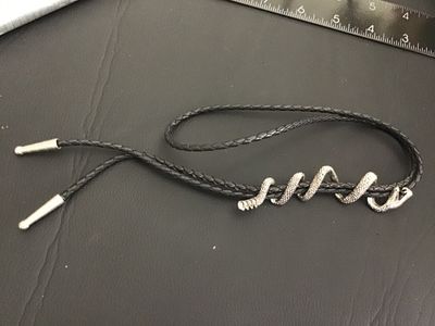 Sale Photo Thumbnail #253: Unique western bolo tie featuring a silver-tone coiling snake slide piece wrapped around a braided black leather/synthetic cord with silver-tone tips. Shows detailed scale texturing and open mouth snake design. Good condition with light wear.
