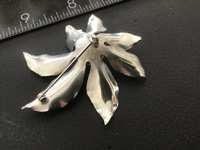 Sale Photo Thumbnail #125: A vintage silver-tone floral brooch Signed  featuring textured, vein-detailed leaves surrounding a domed, textured center. Marked on the back with the copyright Sarah Cov signature. Measures approximately 2 inches wide. Shows minor vintage surface wear co