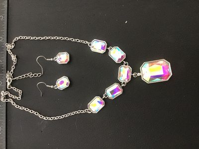 Sale Photo Thumbnail #140: Matching costume jewelry set featuring an iridescent, aura-borealis style emerald-cut crystal stone necklace and coordinating dangle hook earrings in a silver-tone metal setting. Includes a center drop pendant on the necklace with an adjustable chain clos