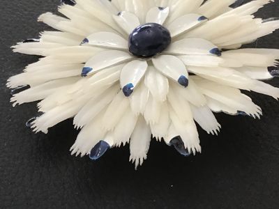 Sale Photo Thumbnail #139: Matching 3-piece vintage jewelry set featuring a large floral brooch pin and two clip-on earrings. Crafted from layered white celluloid petals with painted blue tips and a dark blue center cabochon accent. Brooch measures approximately 3.5 inches across. 