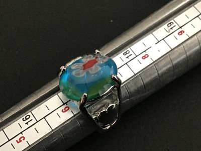 Sale Photo Thumbnail #165: Silver-tone metal statement ring featuring an oval millefiori art glass cabochon in shades of blue, green, white, and red with floral cane details. The band features openwork accents on the sides. Ring is approximately size 7 based on the ring mandrel pho