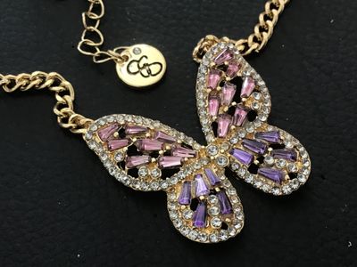 Sale Photo Thumbnail #103: Gold-tone chain necklace featuring a stylized butterfly pendant set with purple, pink, and clear rhinestones. Features a logo hang tag at the clasp extender. Measures approximately 11 inches in total laid-flat length including the pendant. In good pre-own
