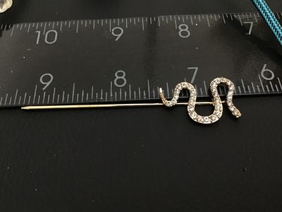 Sale Photo Thumbnail #217: Gold-tone metal stick pin featuring a serpentine snake design encrusted with clear pave rhinestones. Measures approximately 3 inches in total length. Good condition with all stones intact.