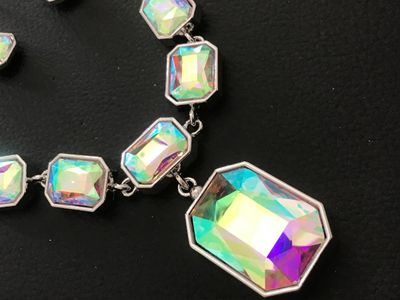 Sale Photo Thumbnail #141: Matching costume jewelry set featuring an iridescent, aura-borealis style emerald-cut crystal stone necklace and coordinating dangle hook earrings in a silver-tone metal setting. Includes a center drop pendant on the necklace with an adjustable chain clos