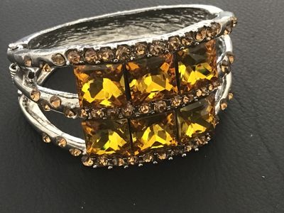 Sale Photo Thumbnail #119: Silver-tone metal hinged cuff bracelet featuring six large square-cut yellow/amber faux crystal central stones bordered by smaller amber-colored rhinestones. Features a spring-hinged closure. Good pre-owned condition with minor finish wear to the reverse.